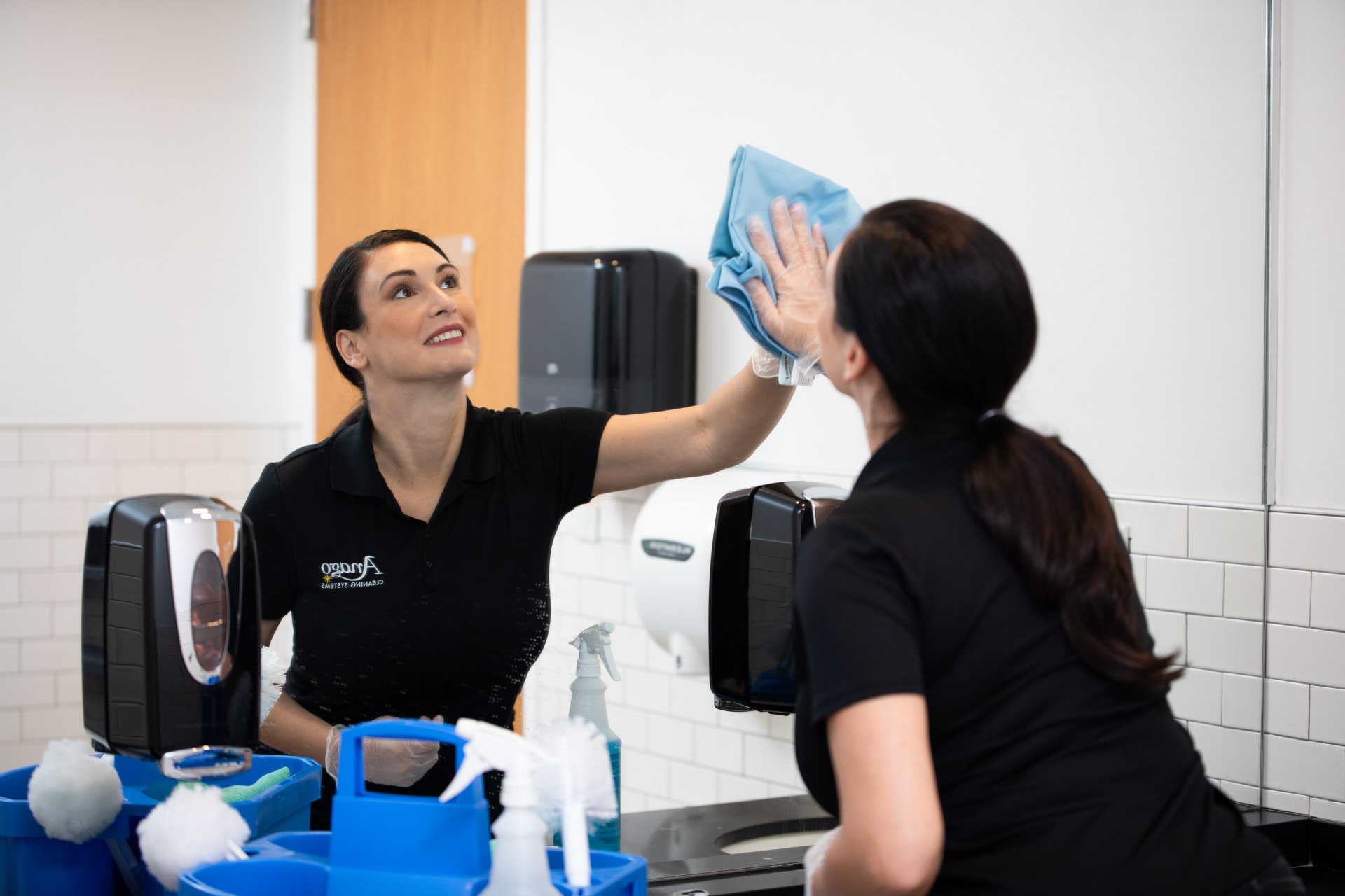 Anago cleaning professionals wiping a restroom mirror and counter