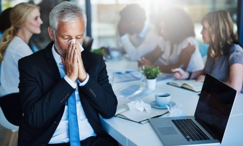 Businessman sneezing into a tissue during a meeting